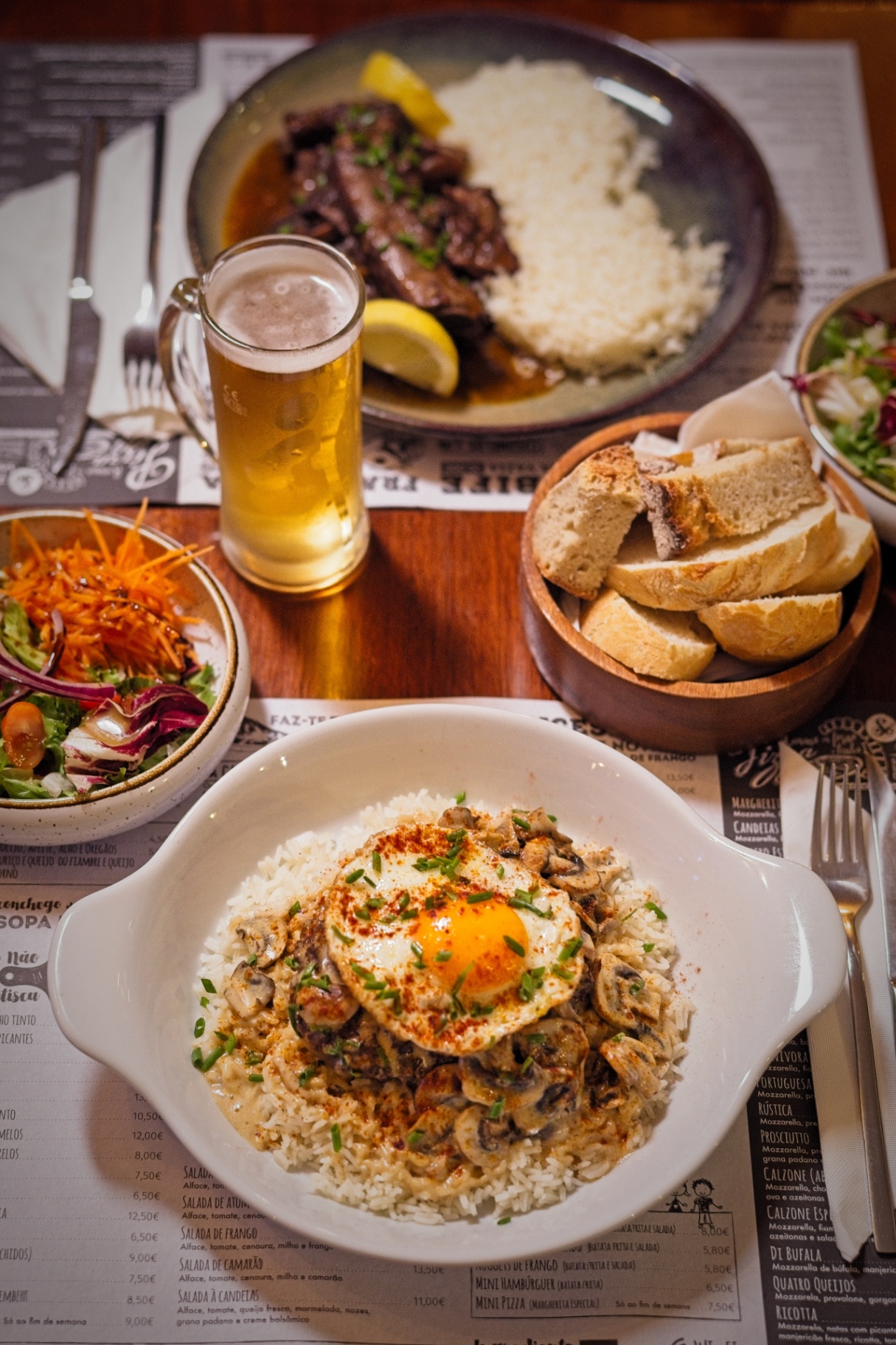 Vista de cima de mesa completa com carne, arroz, salada, pão e cerveja.